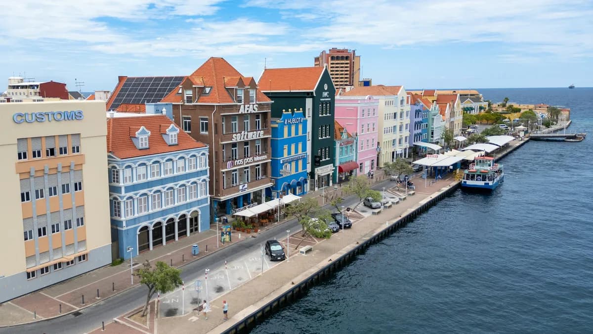 A vibrant waterfront scene in Willemstad, Curaçao, showcasing the iconic colorful Dutch colonial buildings lining the harbor.